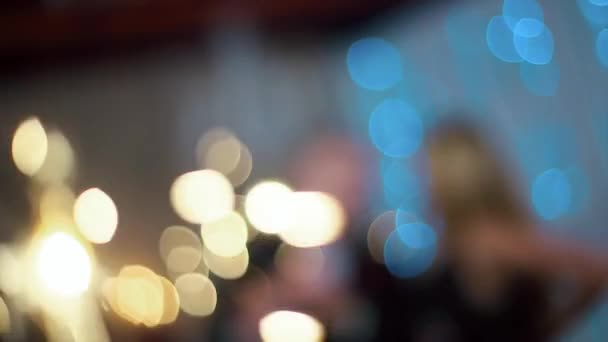 Um homem em um terno preto e uma mulher na noite vestido preto acenando sparklers, em uma sala branca com lareira e árvore de Natal — Vídeo de Stock