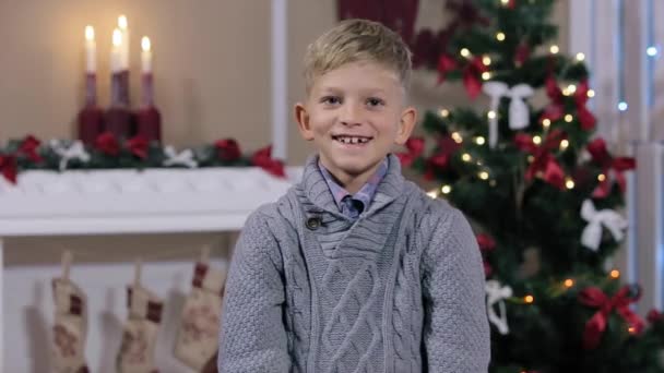 Niño pequeño sosteniendo dos dedos, sonriente, habitación blanca con chimenea y árbol de Navidad, Mediano — Vídeo de stock