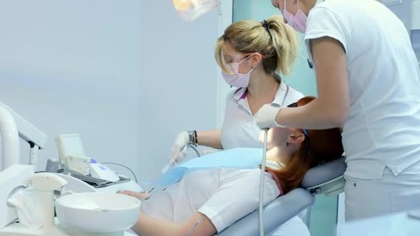 Maskované a rukavicích zubař vysvětluje nadcházející zacházení s jeho pacientka pak začne vyšetření pomocí zubní sondy, pomáhal jeho zubní asistent sací trubice
