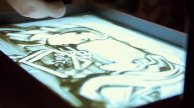 Sanatçı iki kişi kum üzerine çizer.