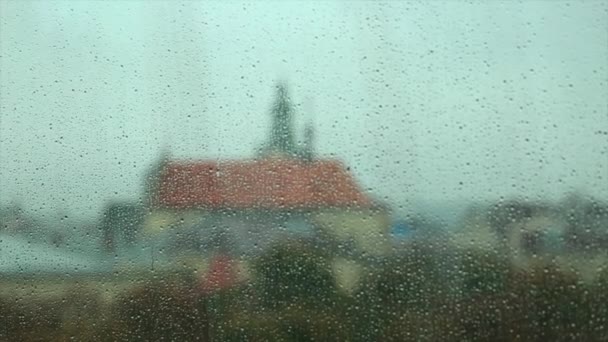 Краплі дощу на склі вікна з розфокусованими будівлями на задньому плані — стокове відео