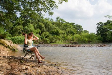 Kız nehrin kenarındaki bankta oturarak güzel bir günbatımının tadını çıkarıyor. Kız açık havada suyun yanında oturuyor. Doğayla birlik. Yalnız kız suya bakar.