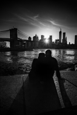 Bir çift bir gün batımını izlemek Hudson Nehri üzerinde Brooklyn Köprüsü ve Manhattan siluetinin aşık.