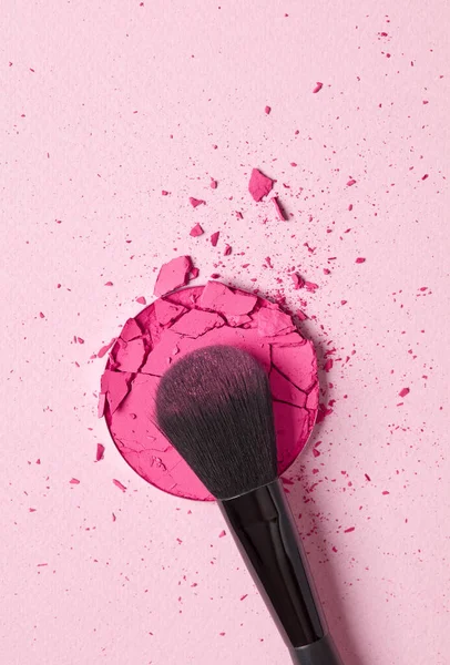 Crushed eyeshadow and brush on pink background