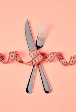 Pembe arka planda mezuralı çatal ve bıçak.