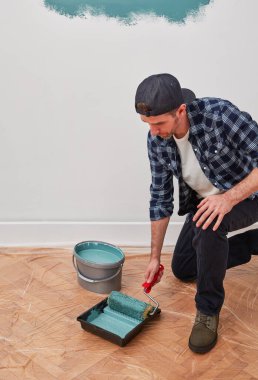 Boya kovası ve boya silindirli bir boyacı.