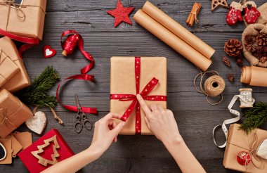 Noel kutularını paketlemek, bir kadının tahta bir masanın üzerine kurdele eklemesi.