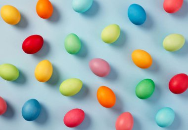Renkli paskalya yumurtaları pastel mavi arka plana saçılmış.