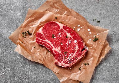 Çiğ pirzola biftek, deniz tuzu ve parşömen kağıdında otlar.