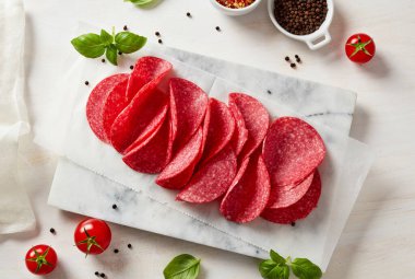 Katlanmış salam dilimleri, fesleğen domatesleri ve mermer tahta manzaralı baharatlar.