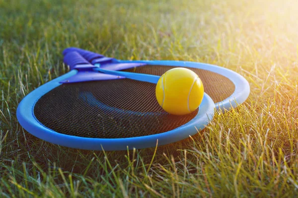 yellow tennis ball on two rackets in park on green grass in summer sunset