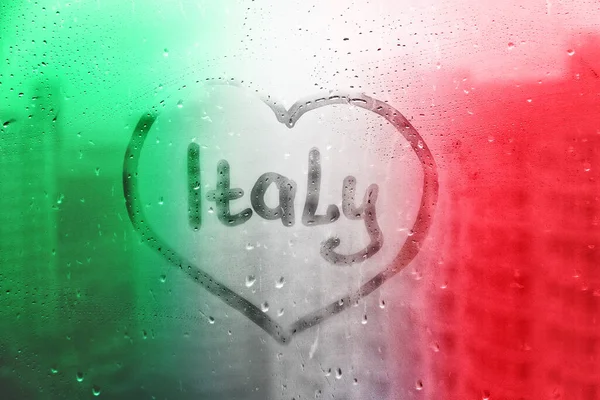 Handwritten word Italy in heart shape on misted window with raindrops in colors of italian flag