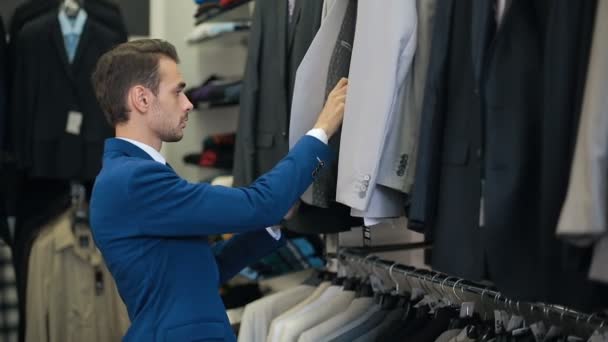 Красавчик выбирает костюм в магазине одежды — стоковое видео