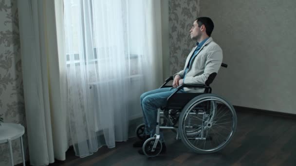 L'uomo su una sedia a rotelle guarda attraverso la finestra — Video Stock