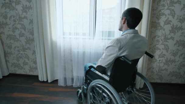 L'uomo disabile su una sedia a rotelle guarda attraverso la finestra — Video Stock