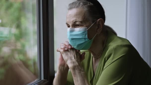 Oudere vrouw met gezichtsmasker bij het raam — Stockvideo