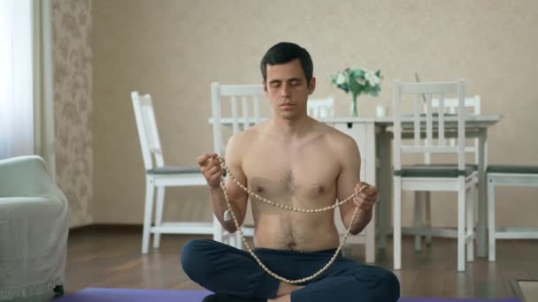 Az ember a gyöngyökön meditál a padlón ülve. — Stock videók