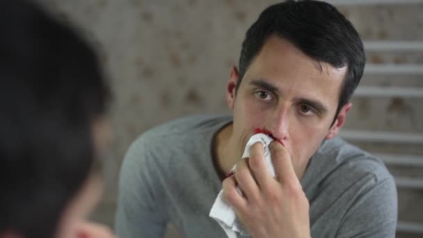 El hombre limpia la hemorragia nasal en un frente del espejo — Vídeos de Stock