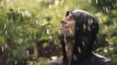Yağmur altında mutlu genç adam yukarı bakıyor