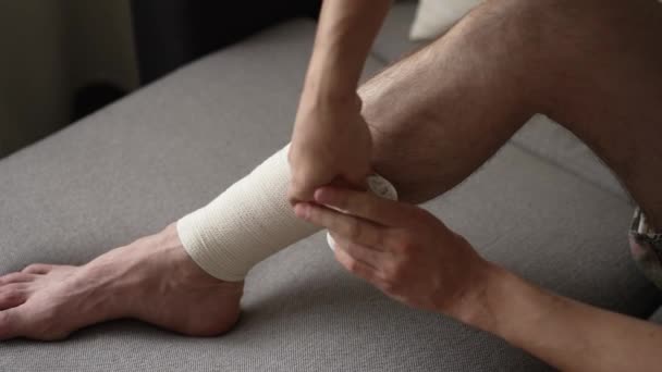 Az ember bekötözi a lábát egy rugalmas kötéssel. — Stock videók
