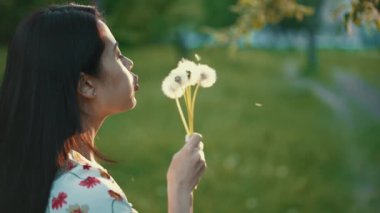 Kadın gün batımında karahindiba üflüyor.