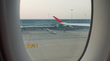 Havaalanı kapısında park halindeyken kabin penceresinden yolcu uçağının kanadının görüntüsü, arka planda terminal binası görünür..