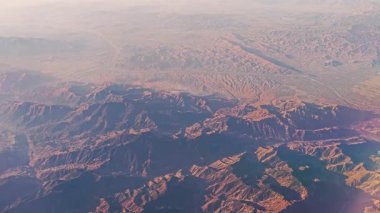 Mars 'ın çorak yüzeyini çağrıştıran, bir uçak penceresinden engebeli, kırmızımsı dağ arazisinin havadan görünüşü.