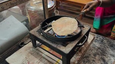Bir aşçı, küçük bir ateşin alevleri üzerinde chapati ekmeği hazırlar ve pişirir..