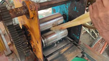 Bir sokak satıcısı taze meyve suyu elde etmek için şeker kamışı saplarını bir el kitabına veya elektrikli öğütücüye dönüştürür..