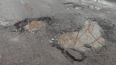 Çatlak ve hasarlı asfalt yüzeyde toplanan su, zayıf altyapı ve hava hasarını gösteriyor..