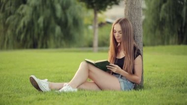 Kadın parkta ağaç tarafından kitap okumak