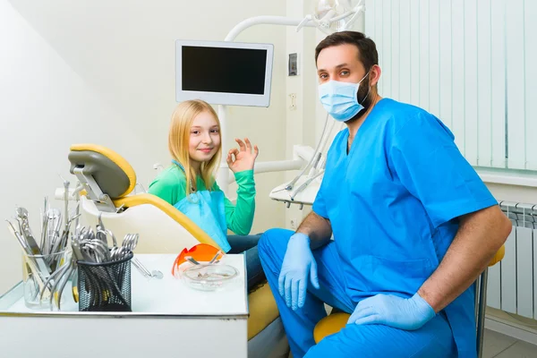 Menina sentada no consultório de dentistas e jogue polegares Ok — Fotografia de Stock