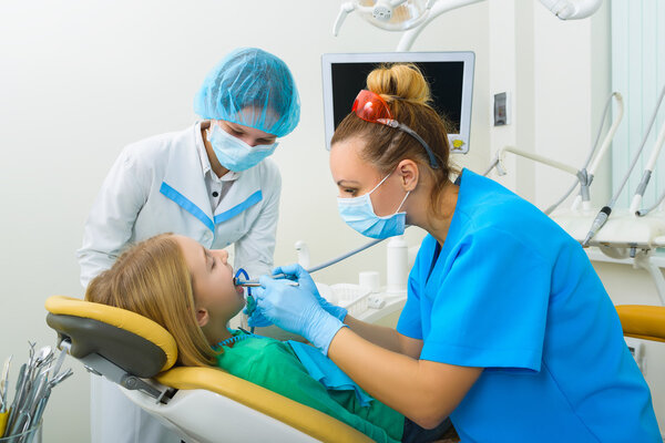 Dentist and nurse making professional teeth cleaning female young patient at the dental office