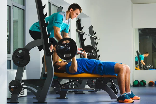 Genç adam içinde spor salonunda egzersiz göğüs üzerinde Bench Press barbell ile — Stok fotoğraf