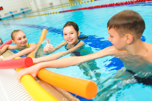 Happy and smiling group of children learning to swim with pool noodle — Stock Photo, Image