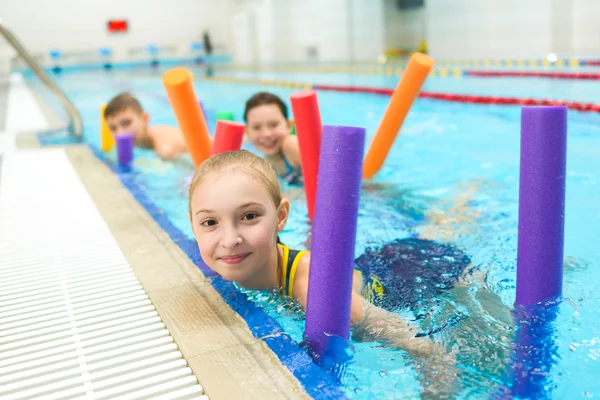 Fröhliche und lächelnde Kinderschar, die mit Poolnudeln schwimmen lernt — Stockfoto