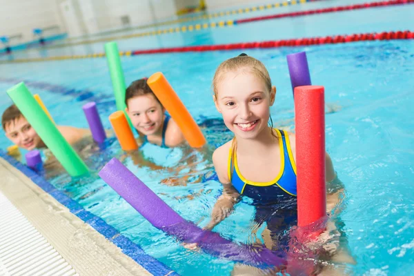 Fröhliche und lächelnde Kinderschar, die mit Poolnudeln schwimmen lernt — Stockfoto
