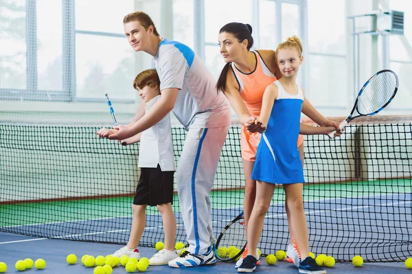 Молодая женщина и мужчина или тренер, обучающие детей играть в теннис на корте — стоковое фото