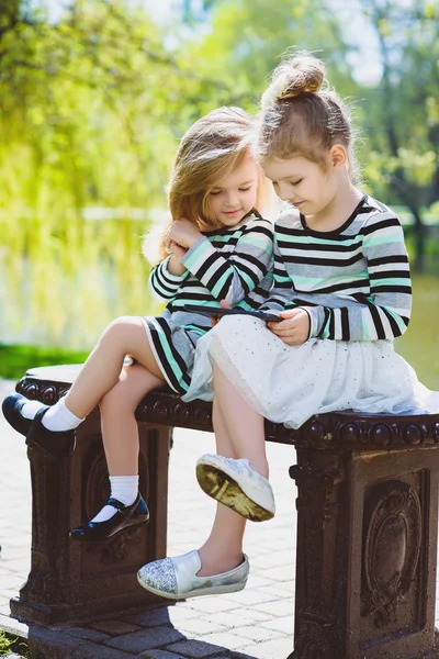 Due ragazze o sorelle bionde felici sedute su una panchina a guardare tablet — Foto Stock