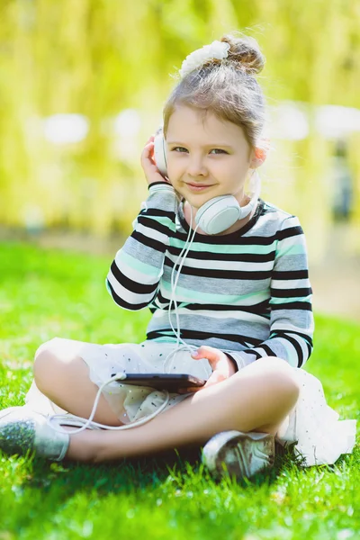 Bambina che ascolta musica con le cuffie in un parco primaverile all'aperto — Foto Stock