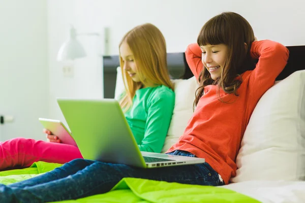 Twee mooie zusjes op bed zitten en spelen met een Tablet of een laptop — Stockfoto