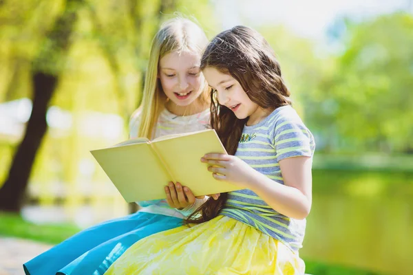 Дети читают книги в парке. Девушки сидят против деревьев и озера на открытом воздухе — стоковое фото
