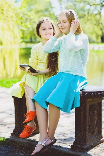 Kleine meisjes luisteren naar muziek op de hoofdtelefoon in een voorjaar park buiten — Stockfoto