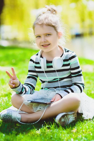 Bambina che ascolta musica con le cuffie in un parco primaverile all'aperto — Foto Stock