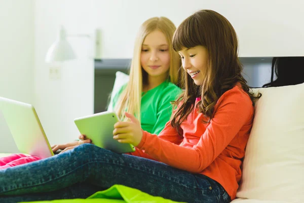 Twee mooie zusjes op bed zitten en spelen met een Tablet of een laptop — Stockfoto