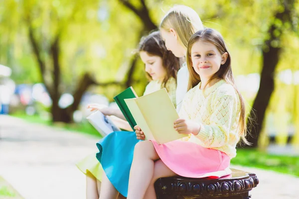 Crianças lendo livros no parque. Meninas sentadas contra árvores e lago ao ar livre — Fotografia de Stock