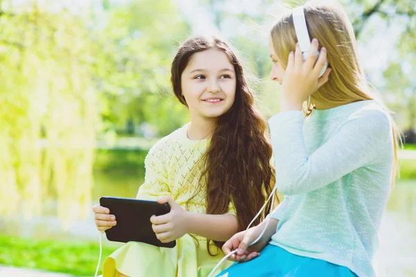 Bambine che ascoltano musica con le cuffie in un parco primaverile all'aperto — Foto Stock