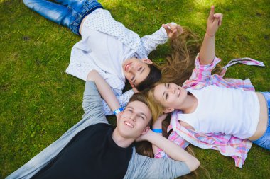 Gülümseyen çocuklar eğleniyor ya da sırtüstü yatıp gökyüzüne bakıyorlar. Yaz aylarında açık havada oynayan çocuklar.