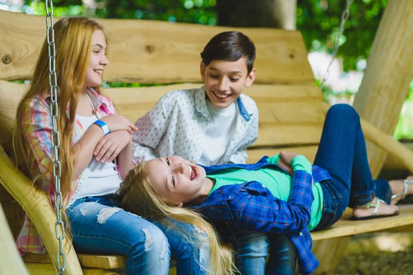 Ragazze e ragazzi sorridenti che si divertono al parco giochi. Bambini che giocano all'aperto in estate. Adolescenti su un'altalena . — Foto Stock