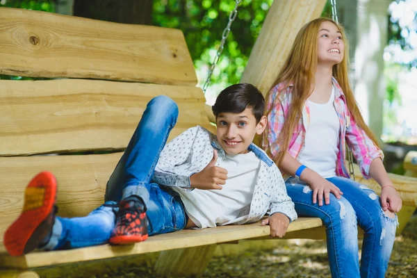 Glimlachend meisje en jongen plezier hebben in speeltuin. Kinderen buiten spelen in de zomer. Tieners op een schommel. — Stockfoto